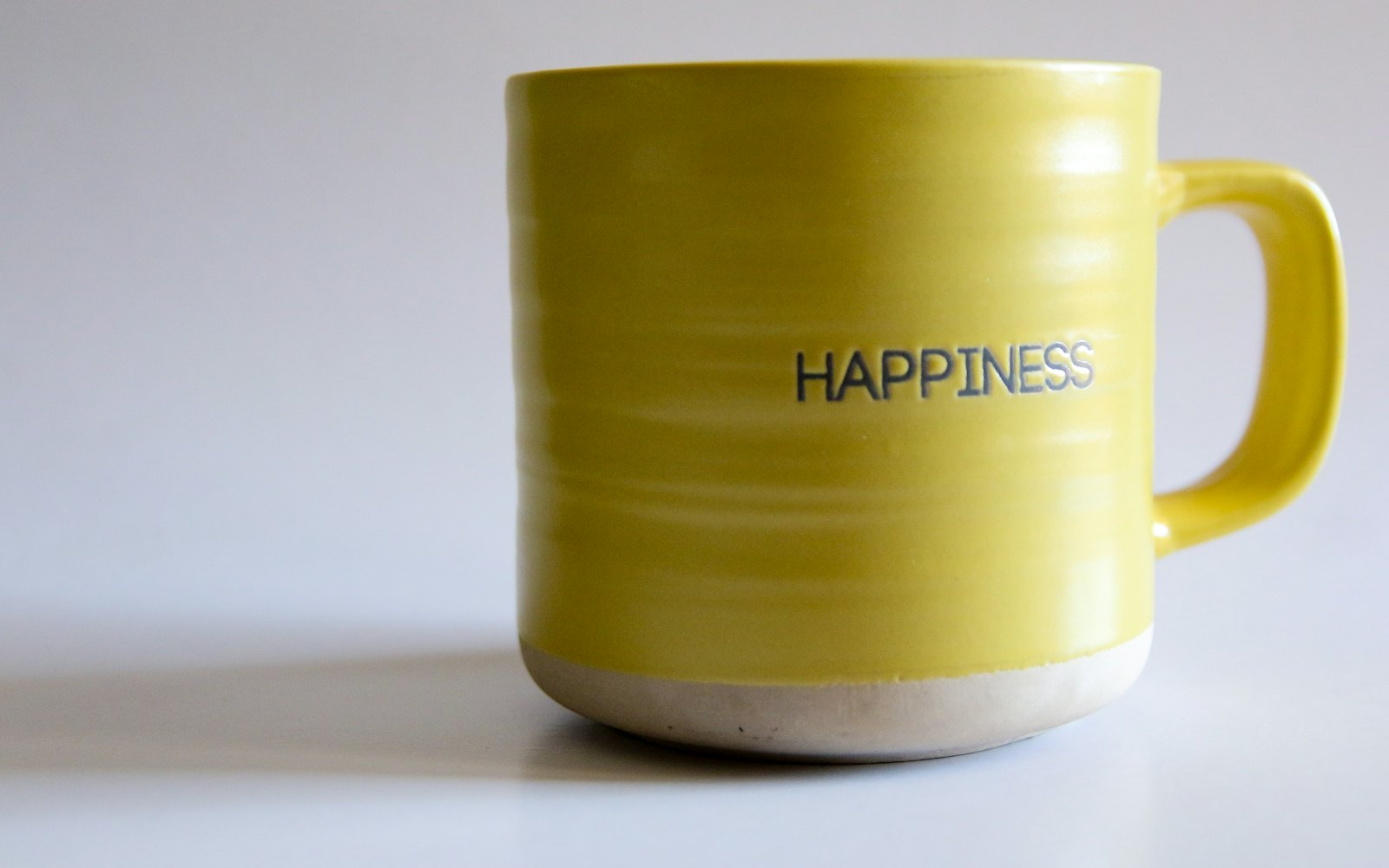 A yellow coffee mug with the words happiness written on it